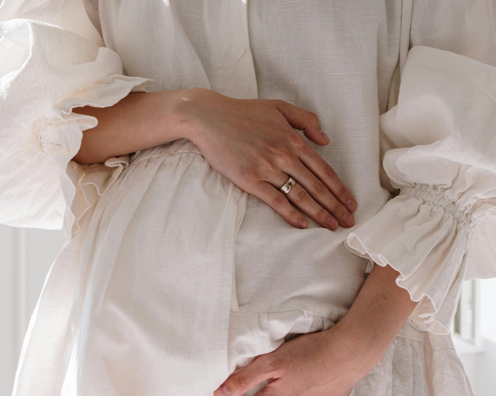pregnant woman wearing a white dress with puffed sleeves, holding their hands together.